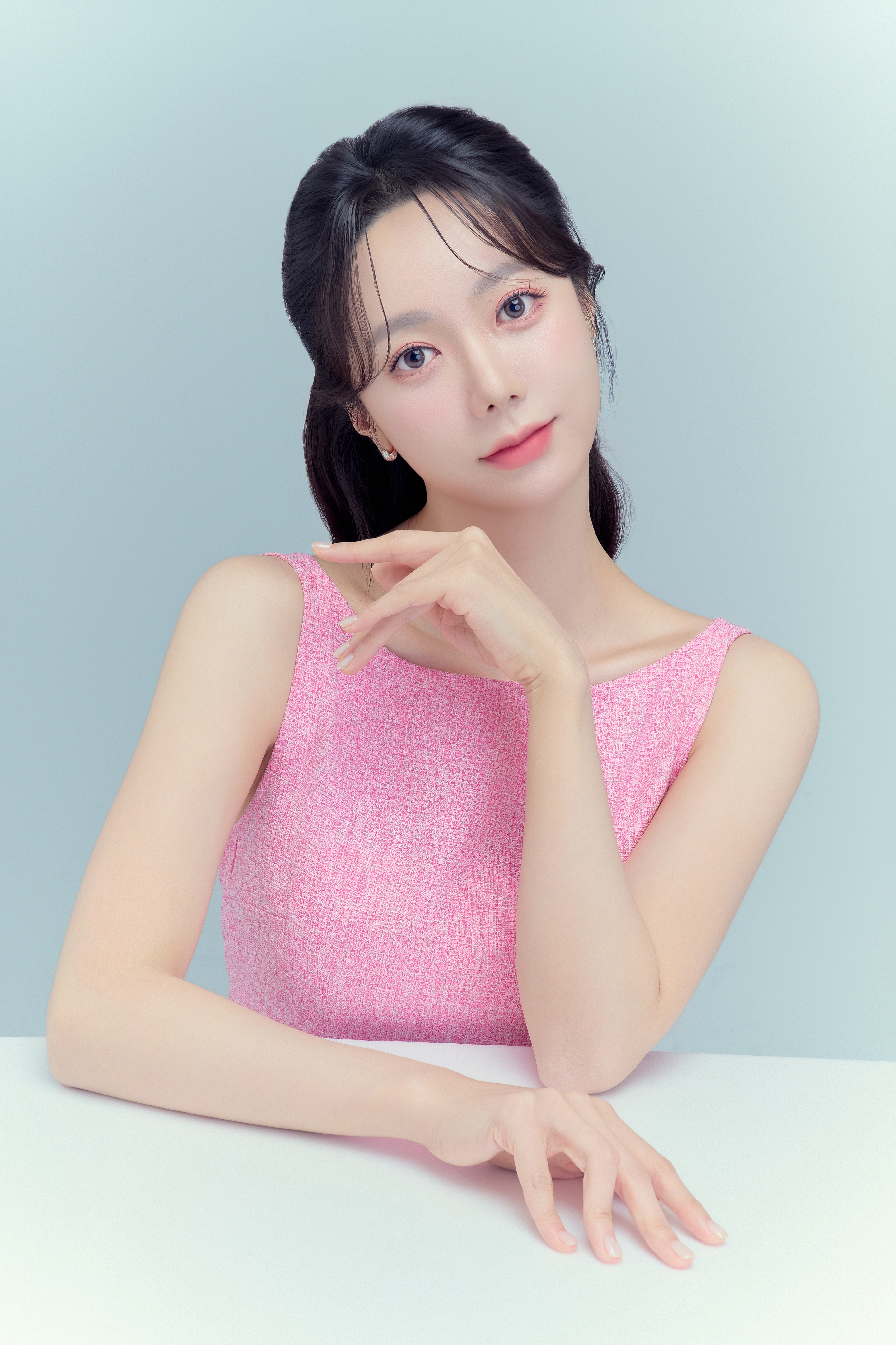 밝은 블루 배경에서 핑크 의상을 입고 테이블에 손을 올린 로얄웍스 인물사진